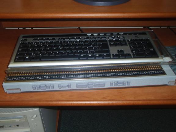 A braille display sitting in front of a computer keyboard on a wooden desk.