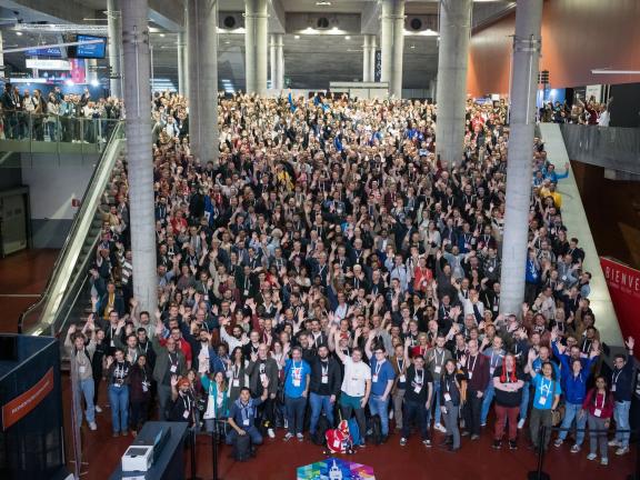 Several hundred attendees waving up at the camera for the group photo at DrupalCon Lille 2023.