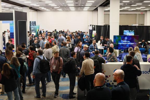 A busy exhibition hall at DrupalCon Atlanta 2025, with attendees talking in groups.