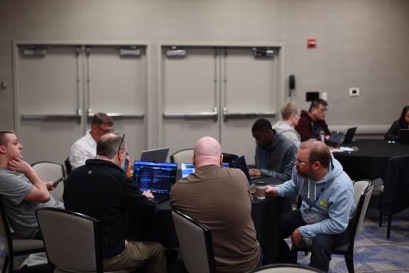 People working on laptops around a table during a training session at DrupalCon Atlanta 2025.