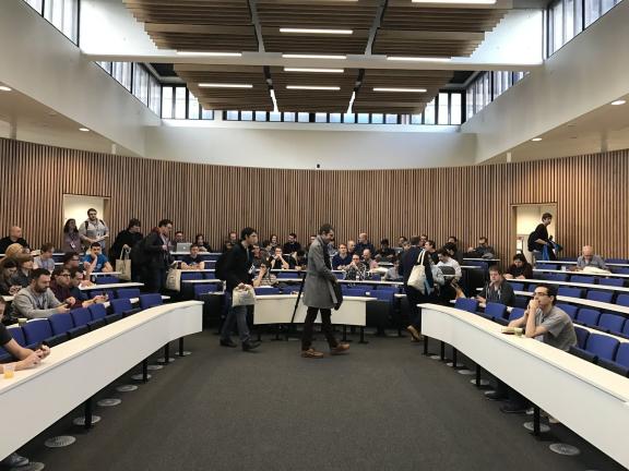 People finding their seats in a tiered lecture theatre at DrupalCamp London 2017.