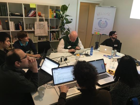 A small team around a table of laptops in a library meeting room, working through a shared screen.