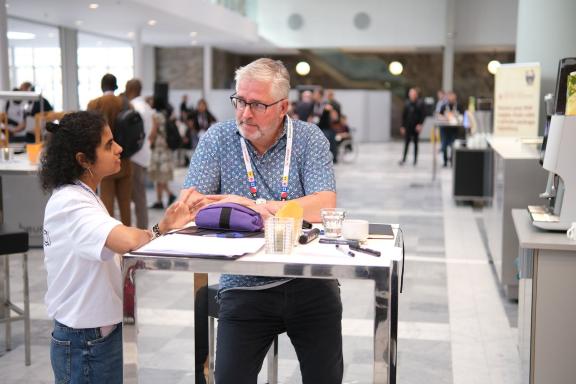 Two attendees talking across a small table in the hall at DrupalCon Rotterdam 2026.