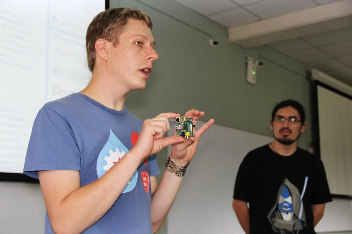 A developer holds up a circuit board while explaining his project