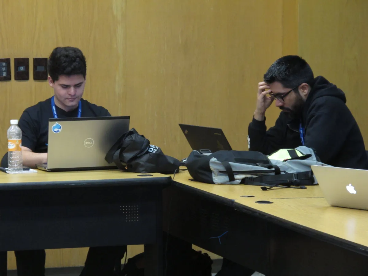 Two developers working side by side on laptops at DrupalCamp México