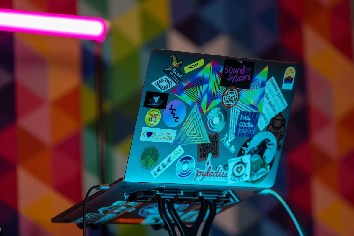 A sticker-covered laptop against a colourful patterned wall at DrupalCon Prague 2022