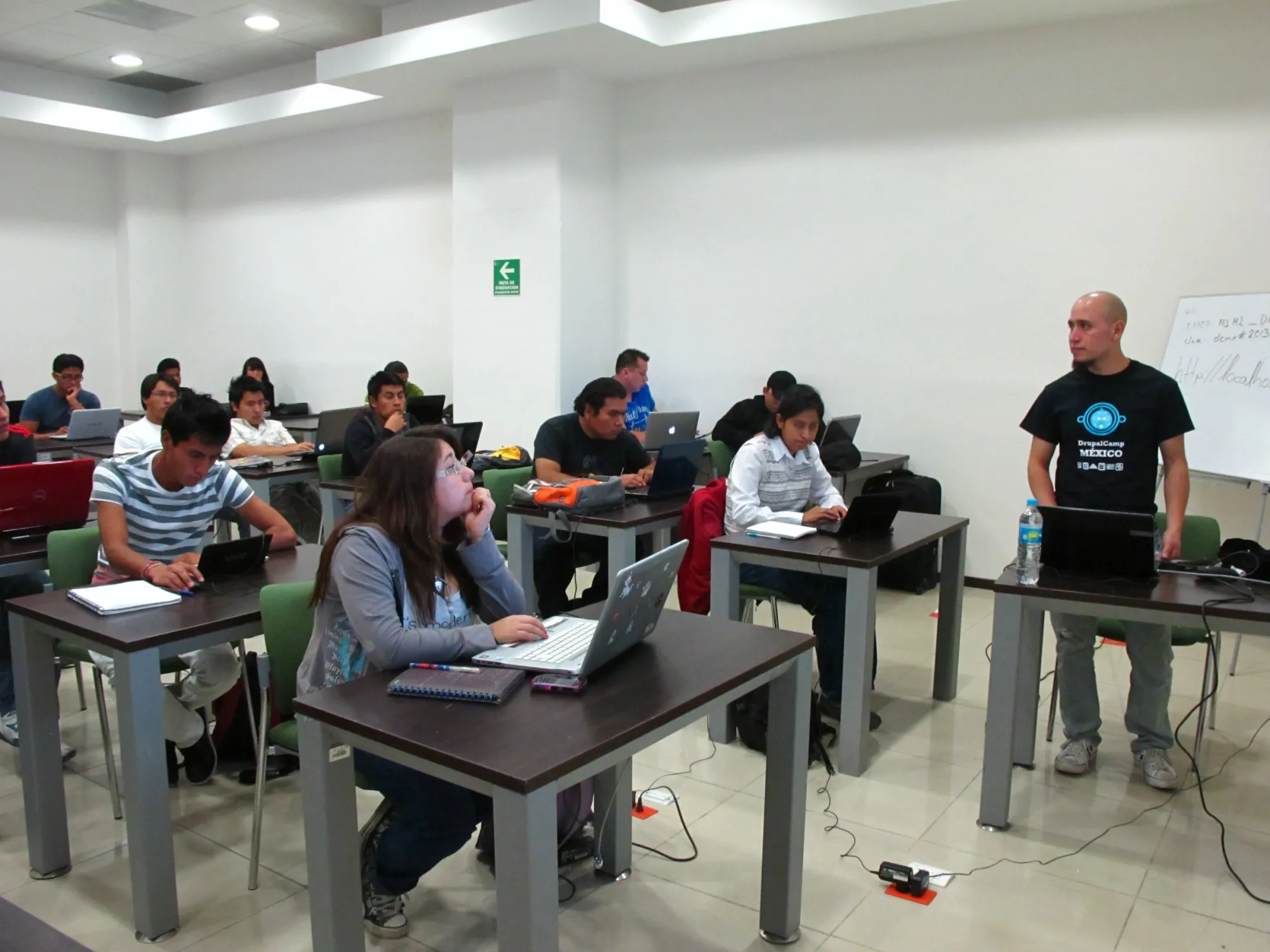 A mentor stands beside people working on laptops in a workshop room