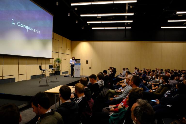 A speaker presents a slide titled "Components" to a large seated audience.
