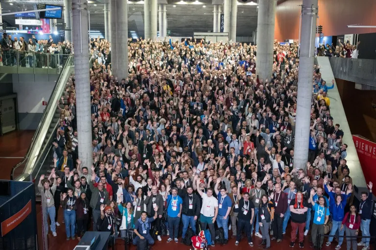 Several hundred attendees waving up at the camera for the group photo at DrupalCon Lille 2023.