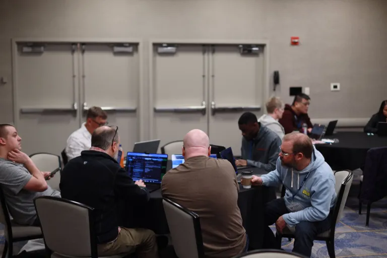 People working on laptops around a table during a training session at DrupalCon Atlanta 2025.