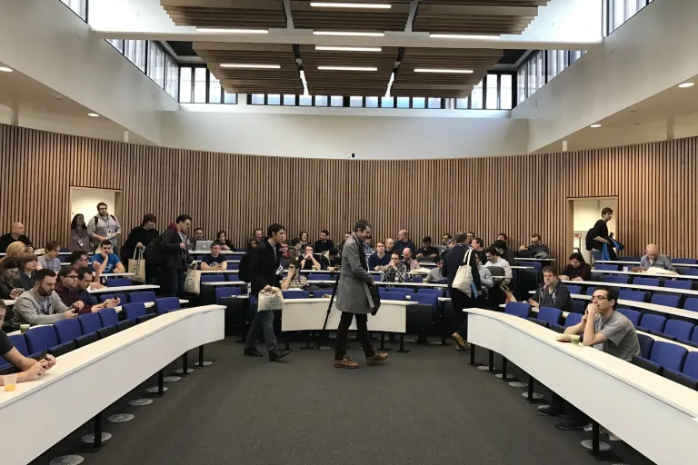 People finding their seats in a tiered lecture theatre at DrupalCamp London 2017.