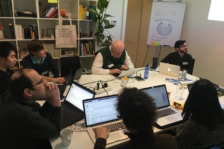 A small team around a table of laptops in a library meeting room, working through a shared screen.