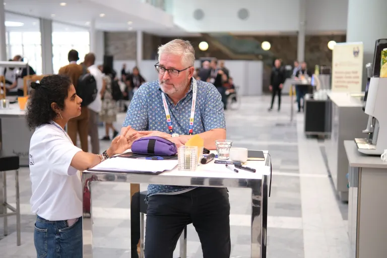 Two attendees talking across a small table in the hall at DrupalCon Rotterdam 2026.