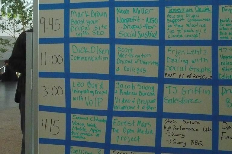 A whiteboard grid of handwritten session sign-ups from an unconference.